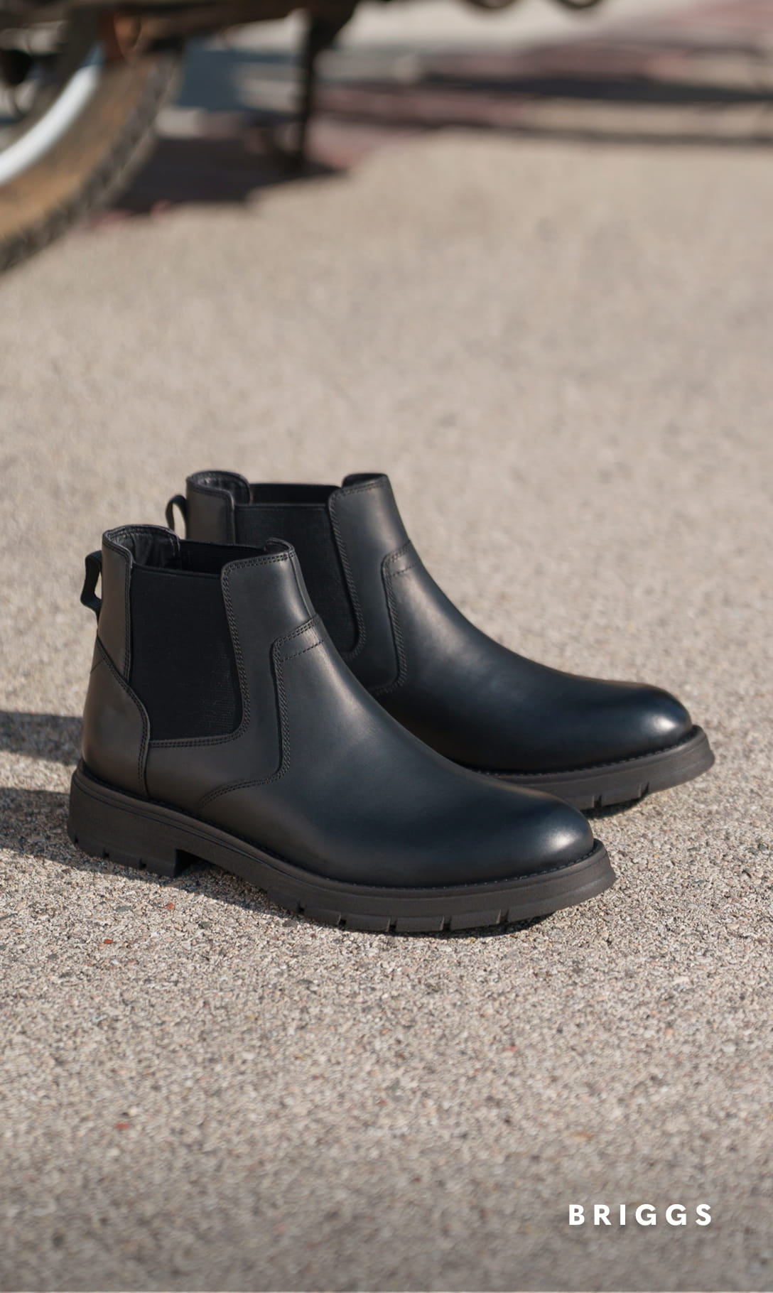 Men's Boots category Image features the Briggs Plain Toe Chelsea Boot in Black Waxy on concrete flooring.