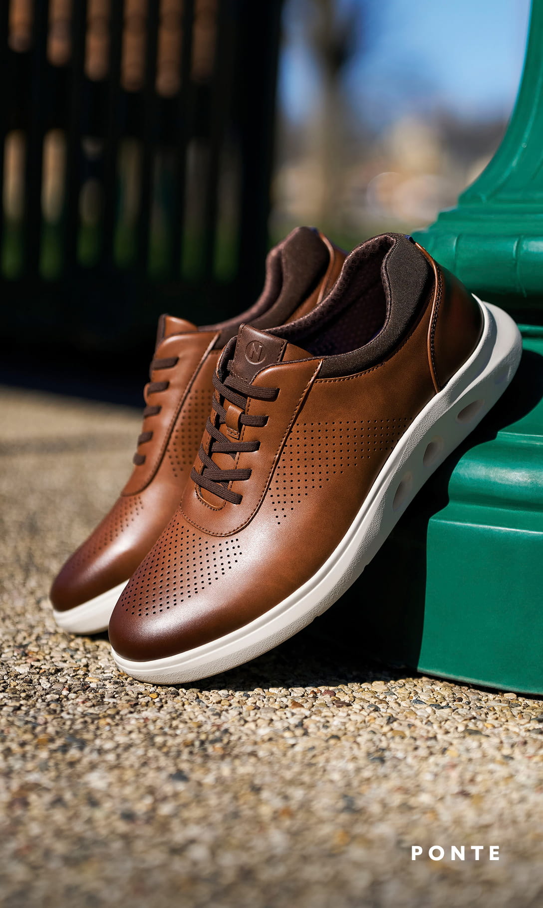 Men's Casual Shoes category Image features the Ponte Perf Toe Sneaker in cognac leaning against a green lamp post.